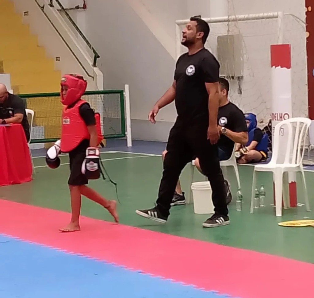 Criança do CT Garagem com equipamento de competição acompanhada pelo professor Wilson Martins
